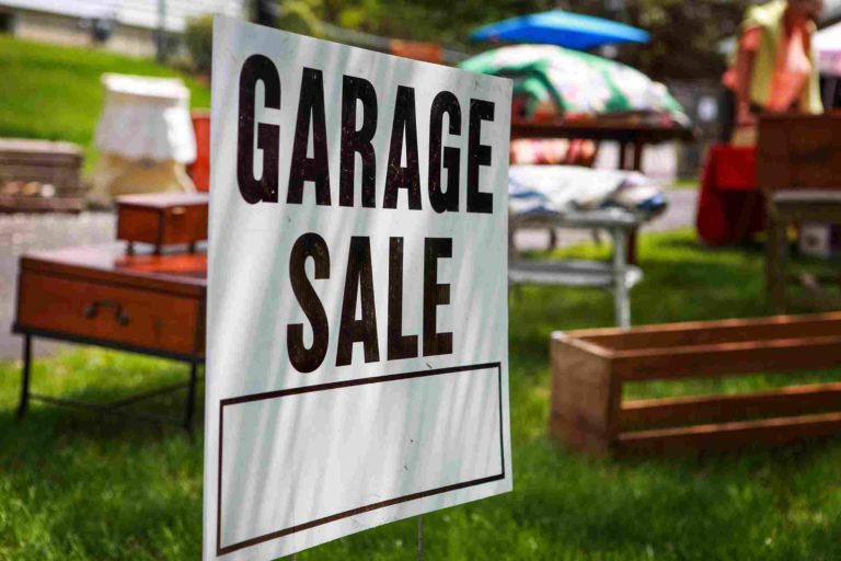 white yard sign with black text reading "Garage Sale" in front of old pieces of furniture on a lawn