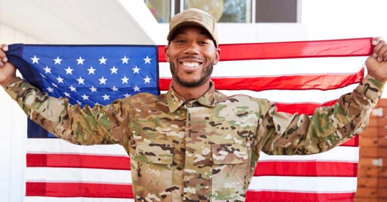 A man in a military uniform is smiling and holding an American Flag.