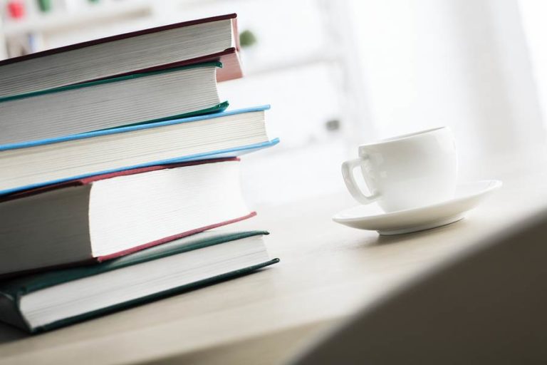 Neatly stacked books next to a warm drink
