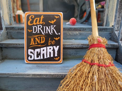 Front porch steps with broom stick, red cake pop, and sign reading “Eat, Drink, and be Scary” leading up to a Halloween party
