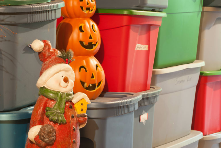 A snowman Christmas decoration and pumpkin Halloween decoration amongst storage boxes that are stacked on top of each other.