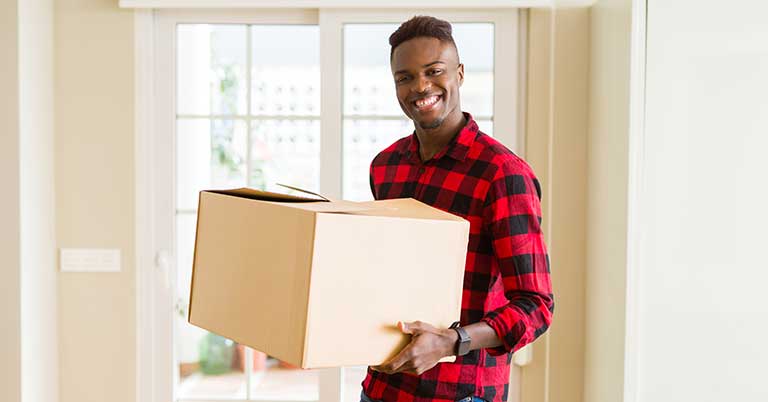 Male in red flannel smiles while he holds a packed cardboard box