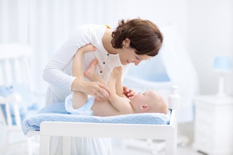 Mother playing with young baby in white room