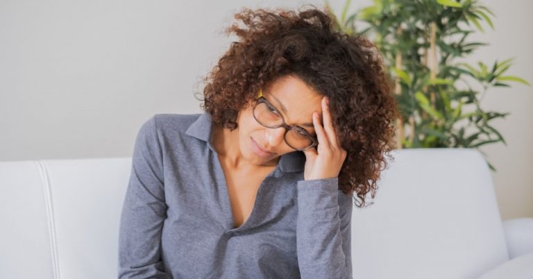 woman sitting on a couch is anxious and resting her forehead on her hand