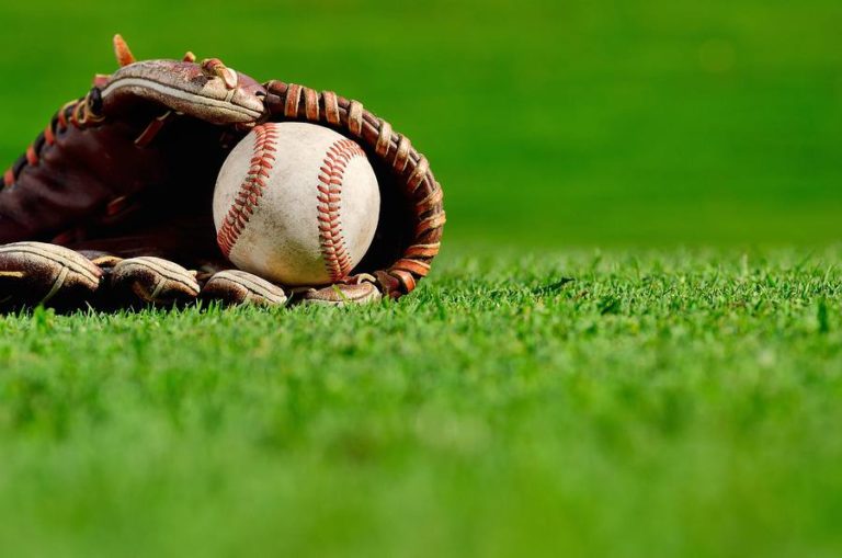 Baseball glove laying in the grass grasping a baseball