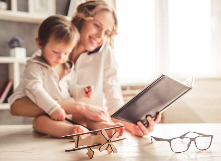 Women holding her kid while reading a book happily