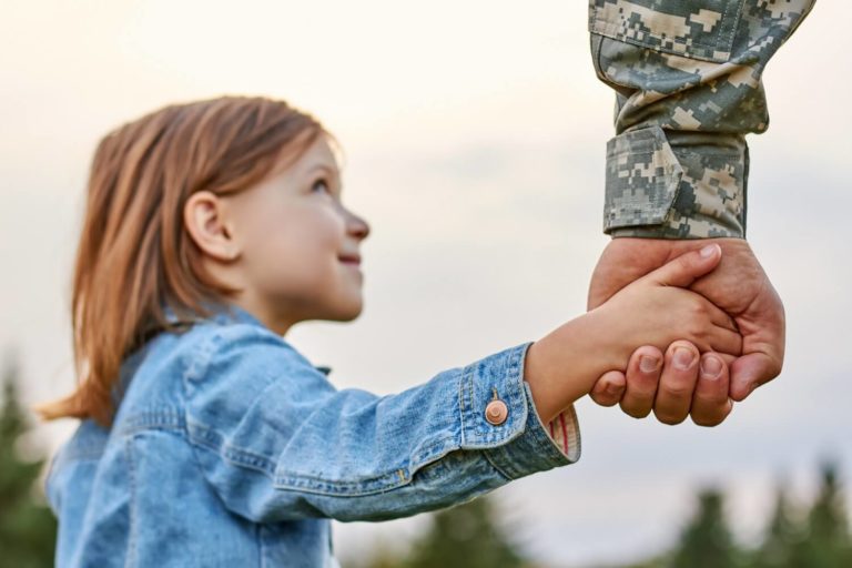 young girl holding the hand of a man dressed in army gear