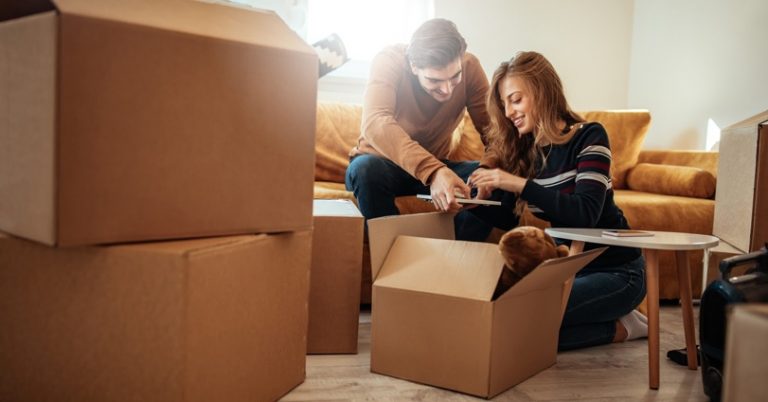 a couple is bent over moving boxes and checking something off a list