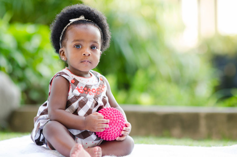 A baby girl sits on the patio in her backyard