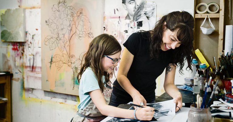 A woman teaching a young girl how to draw.