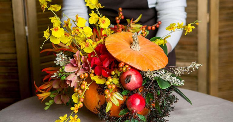 A woman puts the finishing touches on a floral centerpiece made using a carved pumpkin.