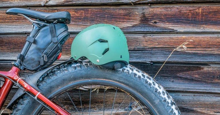 A red bike with a saddle bag on it rests against the side of a wood cabin.