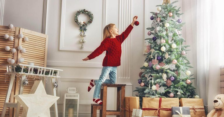 A young girl places an ornament on a Christmas tree.