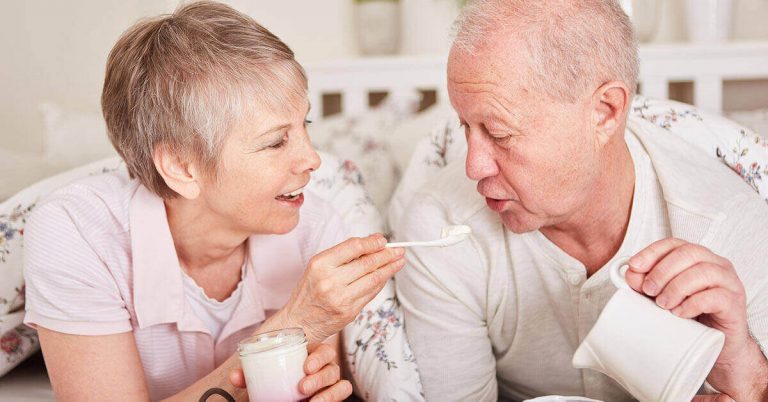 An older couple enjoys breakfast in bed in their hotel room.