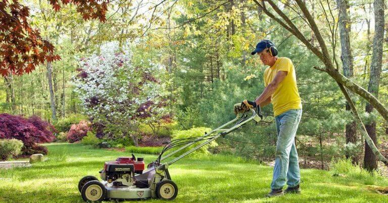 A man mowing his lawn during a sunny summer day.