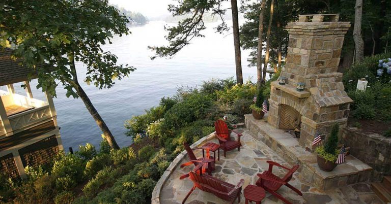 An outdoor fireplace sits on a patio overlooking the lake.