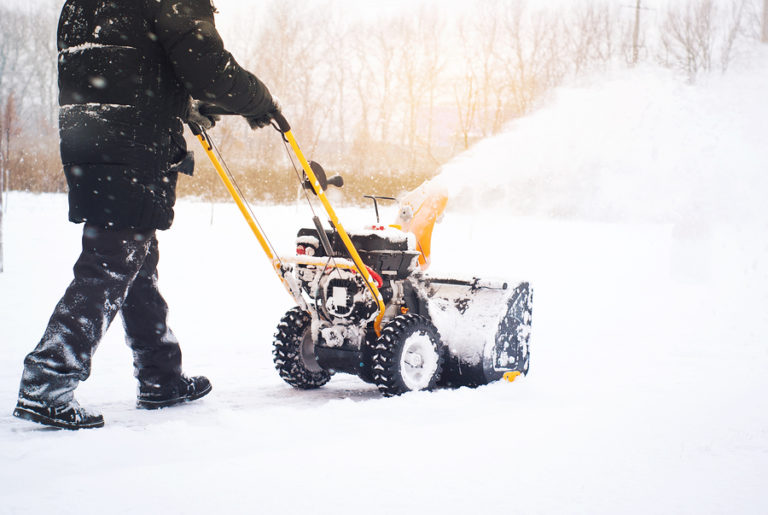 A man pushing a snowblower against a landscape of white.