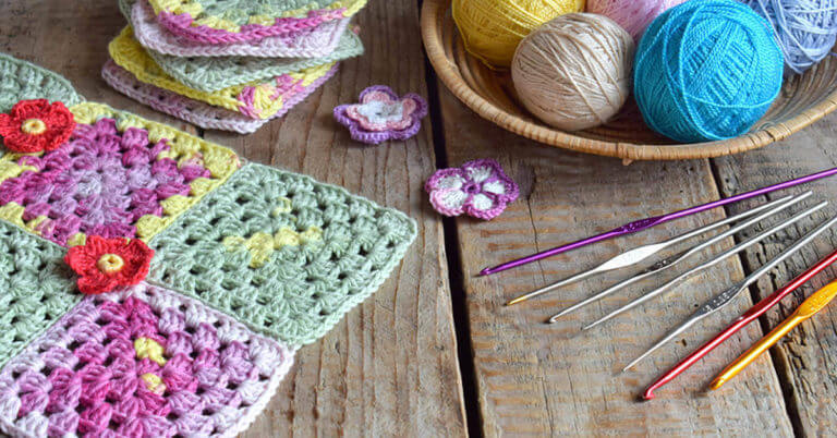 Knitting needles and yarn sit next to crocheted potholders and a blanket.