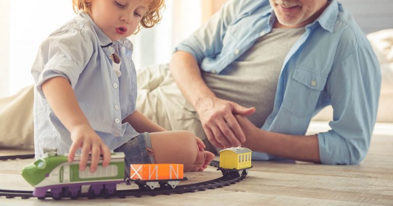 A grandfather plays toy trains with his grandson.