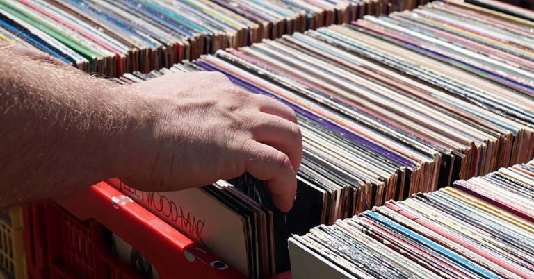 A close-up shot of a manâ€™s hand placing vinyl record albums in storage crates.