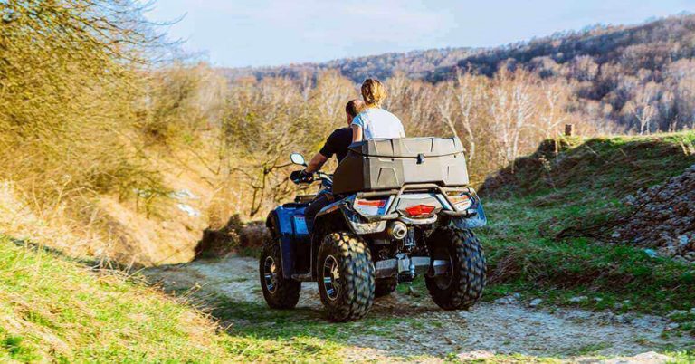 Two people on an ATV ride over a forest hill.