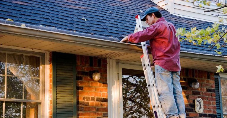 A man uses a ladder to clean his gutters out.