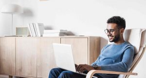 a man working on his computer is sitting in a living room chair by a cabinet