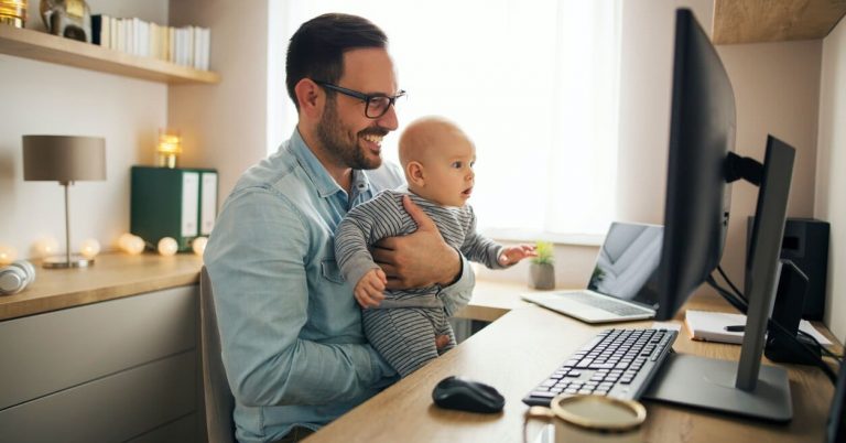 a man holding his infant child sits at his home office in his newly renovated space