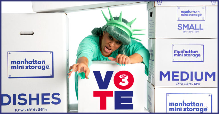 A woman dressed as Lady Liberty climbs over a box that says "VOTE"