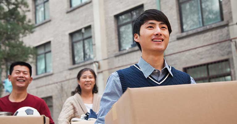 Male student carries a box followed by his parents who both have boxes too