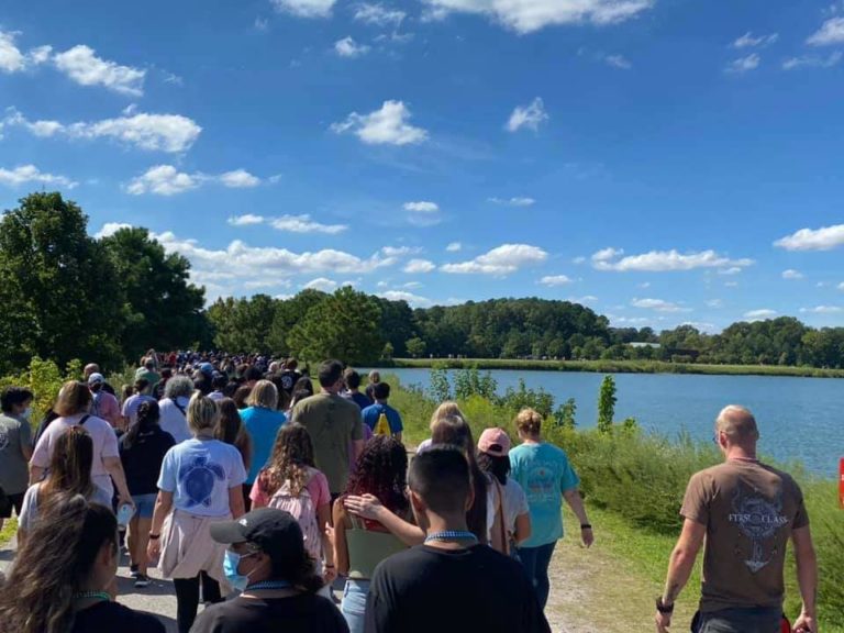 A large crowd of people walking by a lake to raise funds for suicide awareness.