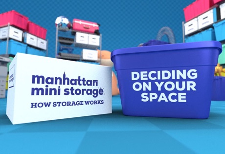 a cardboard moving box on the left reading "Manhattan Mini Storage, how storage works" with a plastic moving box on the right reading "Deciding on your space" with shelves of boxes in the background