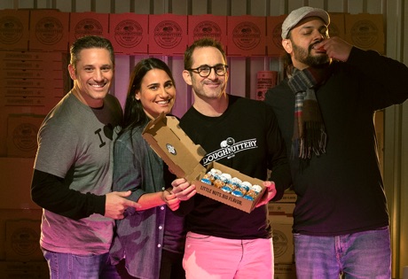 Three people stand next to each other while holding open a box of mini donuts