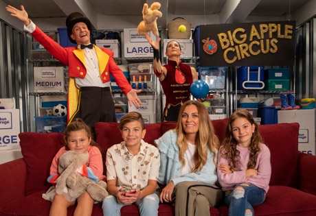 The Manz family sits on a couch with a magician performing behind them.