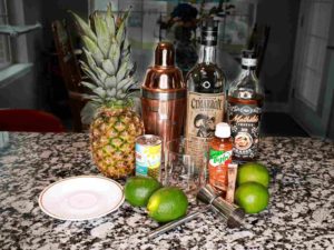 All the ingredients and tools you need for a pineapple margarita are displayed on a kitchen counter. 
