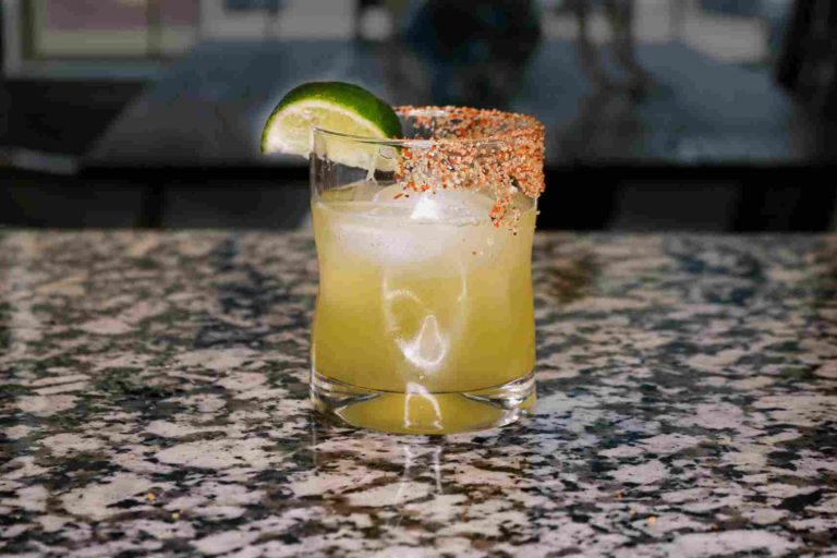 A margarita in a rocks glass sitting on a counter with a salted rim and garnished with a lime