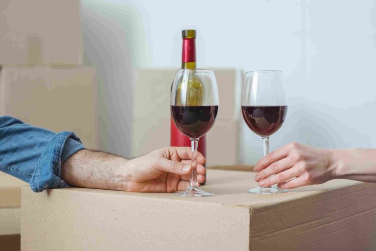 Two hands holding filled wine glasses on a moving box