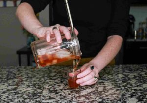 A person pouring the Manhattan Mini cocktail from the mixing glass into a shot glass