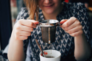 A woman lifts her brewing basket tea infuser out of her mug. 