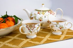 A tea pot and two tea cups on a placemat full of tea. 