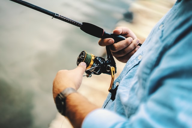 A close up of a person holding a fishing pole and using fishing gear on a dock.