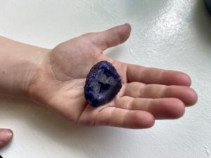 A hand holding a purple geode crystal.