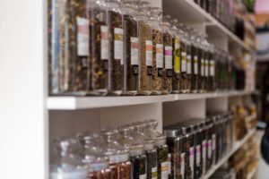 Shelves are lined left to right with large, labeled glass jars of different tea varieties. 